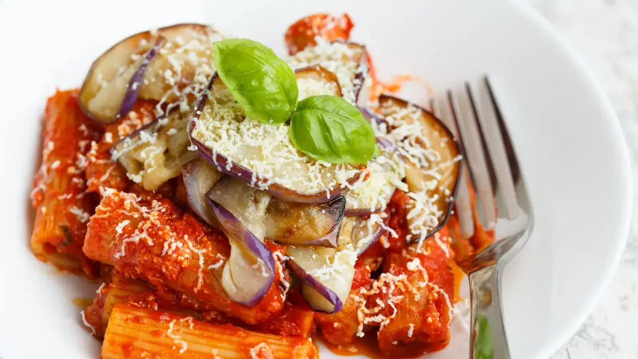 Rigatoni conditi con un saporito sugo alla norma, guarniti con melanzane fritte, ricotta salata grattugiata e foglie di basilico fresco.