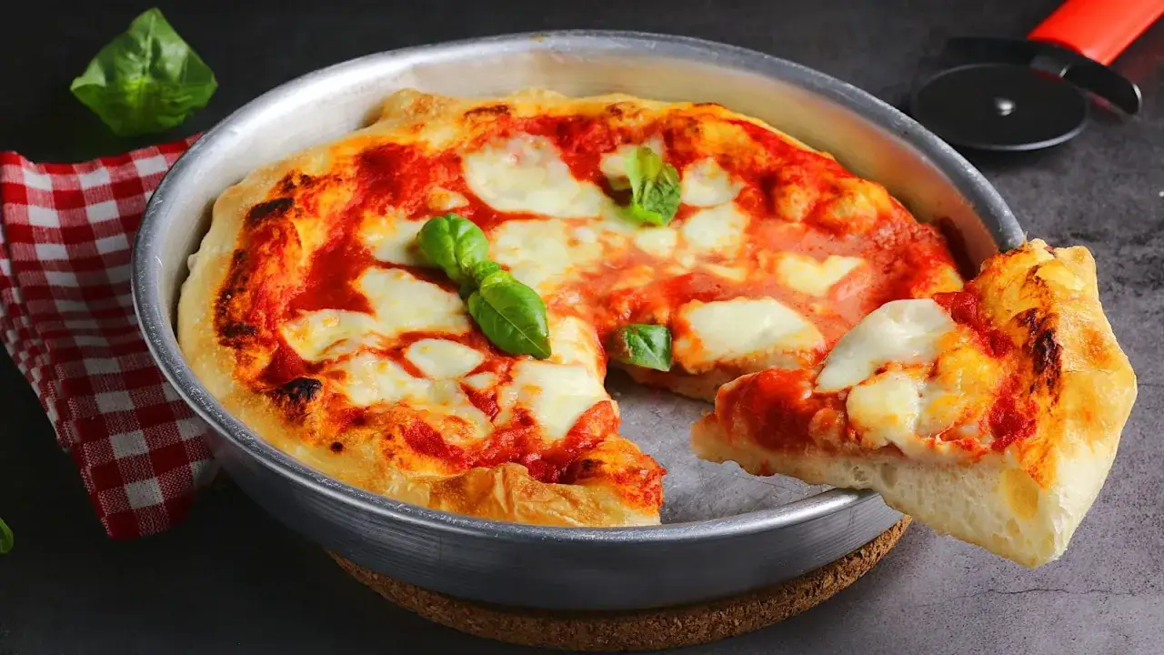Pizza in padellino, calda e filante, con pomodoro, mozzarella e basilico fresco. Una fetta &egrave; gi&agrave; pronta per essere gustata.