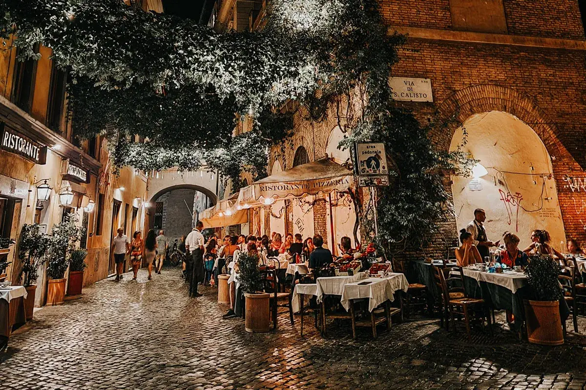 Serata romana: tavoli all'aperto in un vicolo acciottolato, perfetti per scoprire le cose da fare a Roma nel weekend.