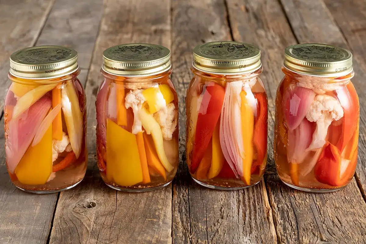 Quattro barattoli di giardiniera in agrodolce, con peperoni, cipolle e cavolfiore, pronti per essere gustati.
