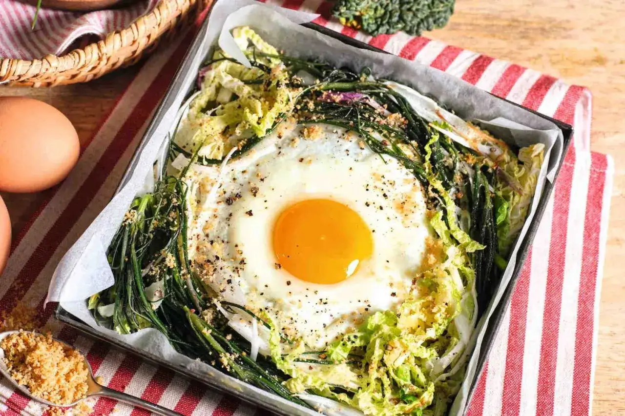 Baked egg in a nest of greens and cabbage, seasoned with pepper and breadcrumbs.