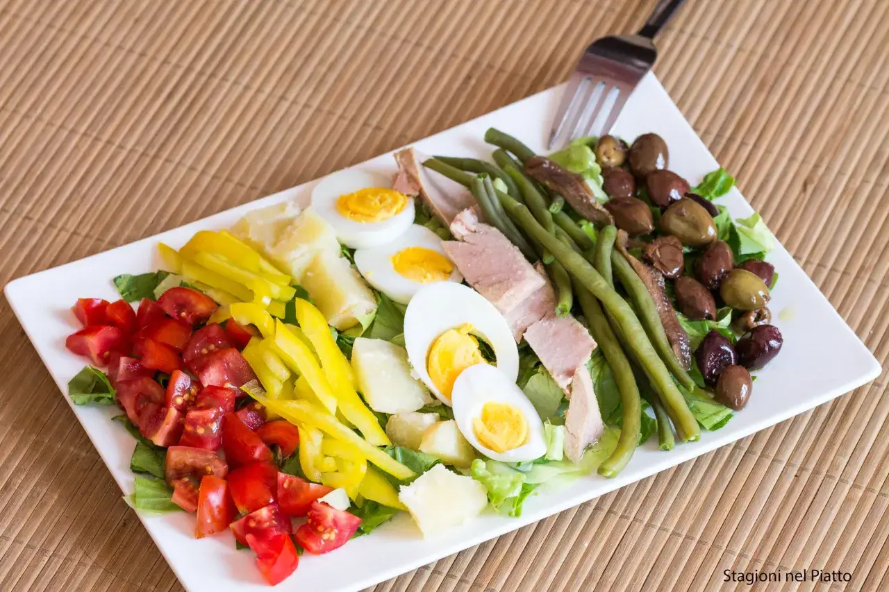 Insalata nizzarda con pomodori, uova sode, tonno, fagiolini, olive e peperoni. Ingredienti freschi e colorati per un piatto gustoso.