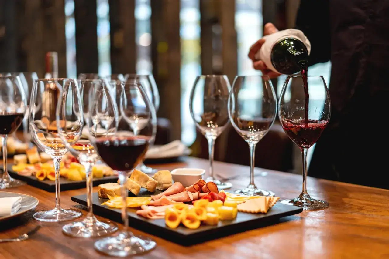 Un sommelier versa vino rosso in un calice, pronto per un perfetto abbinamento cibo vino con taglieri di formaggi e salumi.