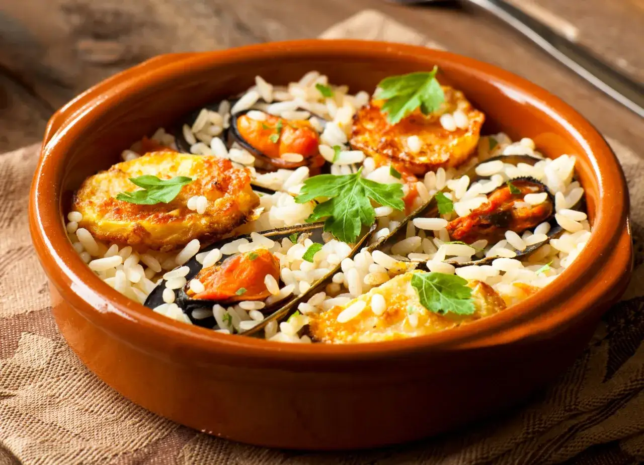 Riso patate e cozze, la ricetta originale pugliese servita in una terrina di terracotta, un piatto ricco di sapori mediterranei.