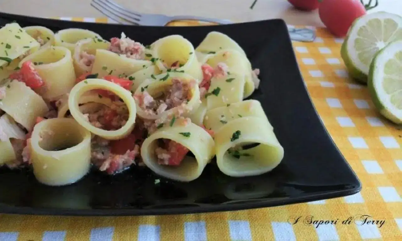 Piatto di pasta con tonno fresco, pomodorini e prezzemolo, guarnito con spicchi di limone.