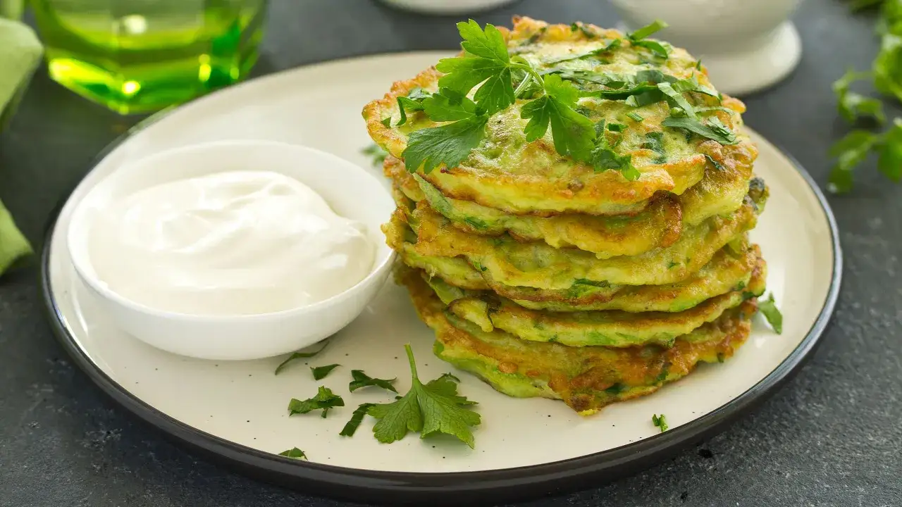 Frittelle dorate di zucchine trombetta, guarnite con prezzemolo fresco, servite con una ciotola di panna acida.