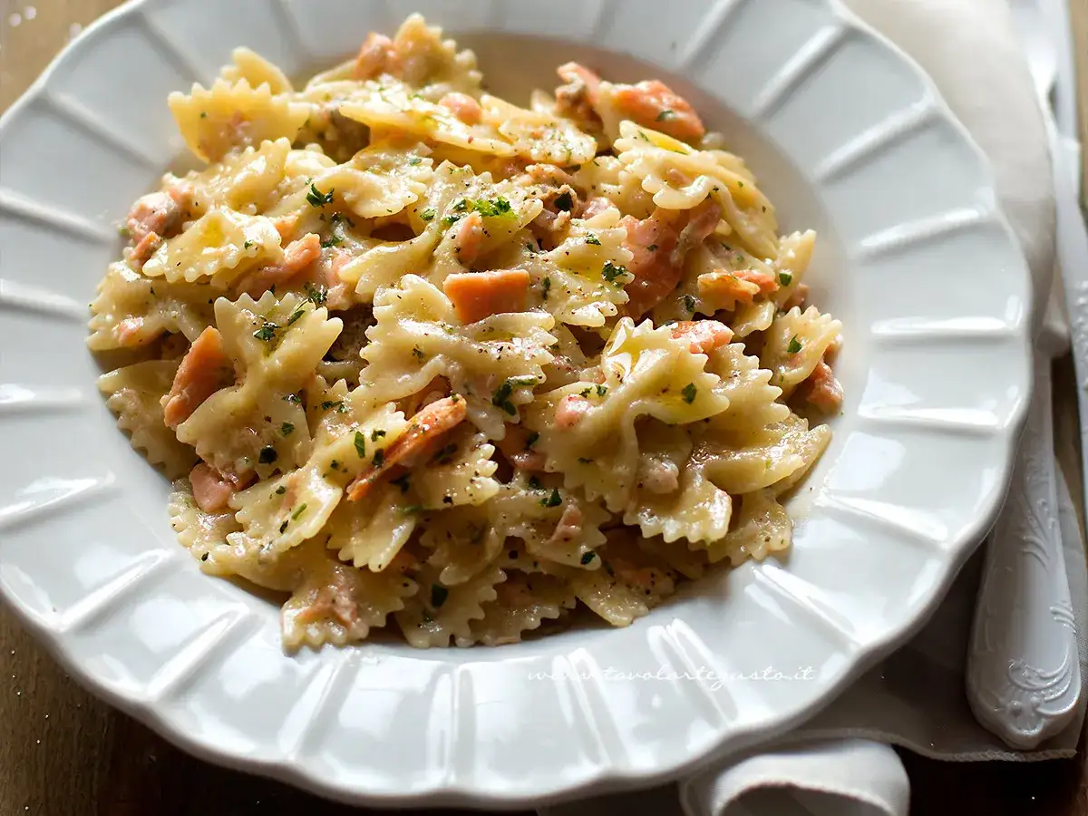 Un piatto invitante di pasta panna e salmone, con farfalle condite in modo cremoso e guarnite con prezzemolo tritato.