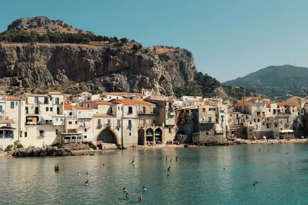 Cefalù, un gioiello da scoprire vicino a Palermo, con case color pastello affacciate sul mare e una rocca imponente.