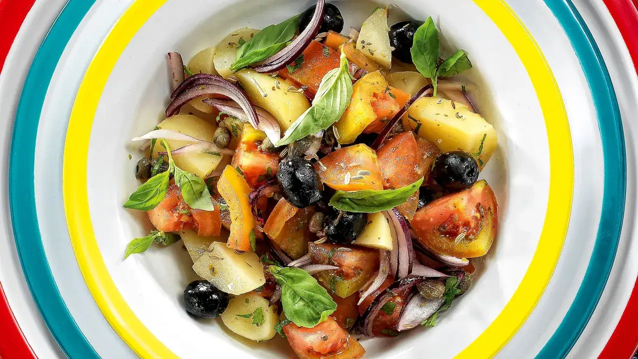 Insalata eoliana con patate, pomodori, olive nere, cipolla rossa e basilico fresco, servita in un piatto colorato.