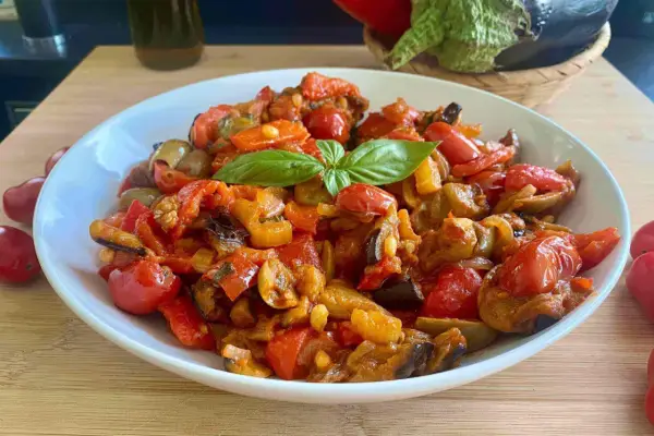 Caponata siciliana ricetta della nonna: un piatto colorato con melanzane, peperoni, pomodorini e basilico, pronto per essere gustato.