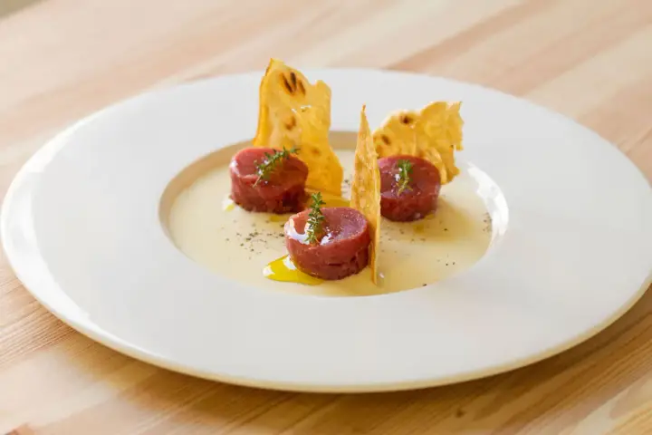 Tre cilindri di tartare di manzo, guarniti con timo, su una crema chiara e croccanti cialde. Un'idea su come condirla.