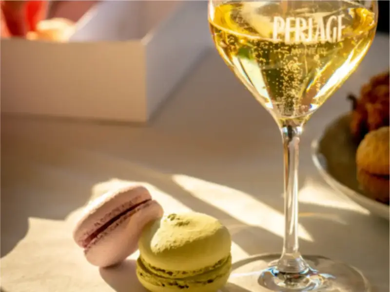 Un bicchiere di spumante frizzante, due macarons colorati e una scatola bianca. Un perfetto abbinamento cibo vino per un momento di dolcezza.