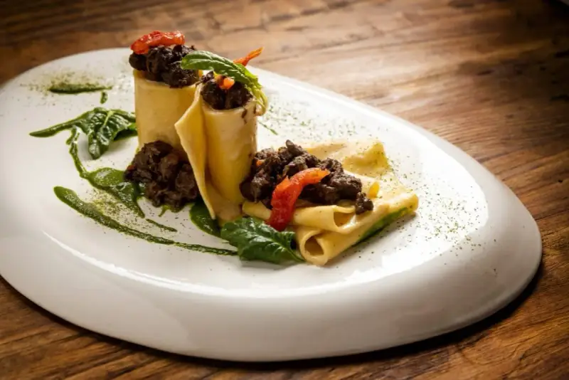 Pappardelle alla lepre, un piatto ricco e saporito, con pasta fresca, ragù scuro e guarnizioni verdi.