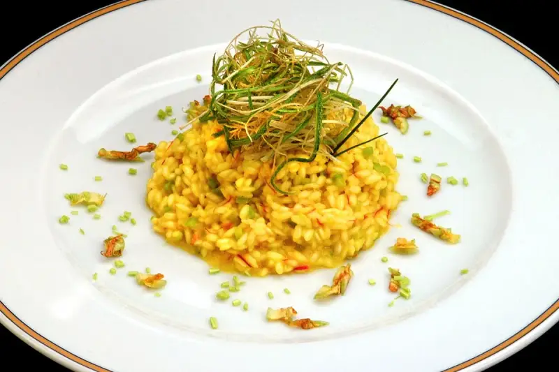 Risotto giallo intenso con fiori di zucca e zafferano, guarnito con erbe croccanti.